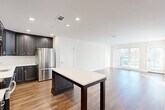 Located at 95 Newport Ave in East Providence, Rhode Island, this well-appointed 2-bedroom, 3-bathroom residence offers a thoughtfully designed single-floor layout. The open-concept living and kitchen area is anchored by a sleek kitchen featuring dark shaker-style cabinetry extending to the ceiling, stainless steel appliances including a refrigerator, range, and microwave, and a large center island with a crisp white countertop ideal for dining or prep. Warm hardwood flooring flows throughout the main living areas, complementing the clean white walls and recessed lighting that create a bright, welcoming ambiance. The living room benefits from oversized windows and direct access to a private balcony, filling the space with abundant natural light and outdoor views. Both bedrooms are generously sized, carpeted for comfort, and well-lit with natural light. The spacious primary bedroom offers ample room and easy access to one of the three bathrooms. The bathrooms are finished with classic black-and-white mosaic tile flooring and clean, neutral fixtures. Three closets throughout the residence, including walk-in storage with built-in wire shelving, provide excellent organizational capacity. The overall aesthetic is modern, clean, and move-in ready.