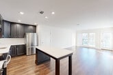 Located at 95 Newport Ave in East Providence, Rhode Island, this well-appointed 2-bedroom, 3-bathroom residence offers a thoughtfully designed single-floor layout. The open-concept living and kitchen area is anchored by a sleek kitchen featuring dark shaker-style cabinetry extending to the ceiling, stainless steel appliances including a refrigerator, range, and microwave, and a large center island with a crisp white countertop ideal for dining or prep. Warm hardwood flooring flows throughout the main living areas, complementing the clean white walls and recessed lighting that create a bright, welcoming ambiance. The living room benefits from oversized windows and direct access to a private balcony, filling the space with abundant natural light and outdoor views. Both bedrooms are generously sized, carpeted for comfort, and well-lit with natural light. The spacious primary bedroom offers ample room and easy access to one of the three bathrooms. The bathrooms are finished with classic black-and-white mosaic tile flooring and clean, neutral fixtures. Three closets throughout the residence, including walk-in storage with built-in wire shelving, provide excellent organizational capacity. The overall aesthetic is modern, clean, and move-in ready.