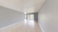 Located at 6919 Bonair Drive in Tampa, FL, this single-story, one-bedroom, two-bathroom home offers a practical and cohesive layout finished consistently with light ceramic tile flooring throughout. The living room is open and airy, featuring a textured ceiling, neutral gray walls, white baseboards, and a sliding glass door that leads directly to the private patio, allowing natural light to flow into the space. Adjacent to the living room, the dining area is defined by a classic pendant light fixture and a window fitted with horizontal blinds, creating a bright and functional space for everyday meals. The kitchen features white cabinetry, white appliances including a range, dishwasher, and full-size refrigerator, along with a single-basin sink and a tile backsplash, providing efficient use of the available space. The bedroom is comfortably sized, painted in the same soft gray tone consistent with the rest of the home, and includes a dedicated closet and a window overlooking the exterior. Both bathrooms are well-appointed; one includes a tub-shower combination, a white vanity with granite countertop, and tile flooring. The home maintains a clean, uniform aesthetic throughout with gray walls, white trim, and textured ceilings, offering a functional living environment in a convenient Tampa location.