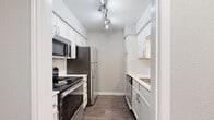 Located at 7350 Brompton Rd in Houston's 77025 corridor, this single-floor residence offers a thoughtfully designed layout with one bedroom, one bathroom, and dedicated closet space. The galley-style kitchen is a functional highlight, featuring white shaker cabinetry, subway tile backsplash, stainless steel appliances including a refrigerator, electric range, microwave, and dishwasher, all set over rich dark hardwood-style flooring with track lighting overhead. The open living area is carpeted in warm neutral tones, providing a comfortable, versatile space that connects seamlessly to the kitchen via a pass-through opening. The generously sized primary bedroom benefits from natural light through multiple windows, plush carpeting, and a ceiling fan for year-round comfort. It connects directly to a spacious walk-in closet outfitted with built-in shelving and hanging rods for ample storage. The bathroom is clean and well-finished, with large-format tile surrounding the tub-shower combination, a white vanity with a light countertop, and dark hardwood-style flooring that ties back to the kitchen aesthetic. Neutral gray walls throughout lend the home a cohesive, modern feel.