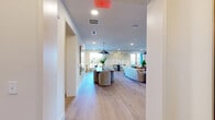 The Sky Lounge in Vestavia Hills, Alabama is a elegantly appointed single-floor communal space that seamlessly blends modern design with warm, welcoming aesthetics. Wide-plank light oak hardwood flooring flows throughout, creating visual continuity across every area.

Upon entry, a well-appointed hallway greets visitors with curated wall art, leading into the open-concept main area. The spacious kitchen features sage-green cabinetry, a subway tile backsplash, stainless steel appliances, and a large central island with a dark countertop and bar seating — ideal for casual gatherings. Pendant lighting with dark metal accents lends an elevated, contemporary feel.

The open living and dining zone is anchored by a substantial dining table beneath a striking pendant light, surrounded by upholstered chairs. A hand-painted tree mural serves as a signature accent wall, adding artistic depth to the space. The lounge area offers comfortable leather seating arranged around a wall-mounted display, with direct access to an outdoor terrace through glass-paned doors that invite abundant natural light.

A private meeting room, distinguished by floor-to-ceiling wood panel walls and a round table with leather chairs, provides an intimate setting for focused conversations. Two bathrooms, a closet, and a dedicated entrance round out the functional layout, making this lounge a versatile and refined destination.