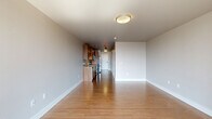 Located on the fifth floor at 53–99 Thomas St in Seattle's Queen Anne neighborhood, Unit 506 is a thoughtfully designed, single-floor residence that makes efficient use of its compact footprint. Warm wood-style flooring runs throughout the unit, lending a cohesive, welcoming feel to every room.

The open-concept kitchen and living area forms the heart of the space. The kitchen is well-appointed with rich, warm-toned wood cabinetry extending to the ceiling, light stone countertops, a subway tile backsplash, and a full suite of stainless steel appliances, including a refrigerator, range, microwave, and dishwasher. Track lighting overhead adds a modern touch. The living area is bright and airy, anchored by a large floor-to-ceiling window that floods the room with natural light and offers views of the surrounding Seattle cityscape.

The bathroom features a full soaking tub with shower, clean white surround with built-in shelving, neutral tile flooring, and warm wood cabinetry above for ample storage. The unit also includes a dedicated closet, providing practical storage solutions. Crisp white walls and clean architectural lines throughout give the residence a fresh, modern aesthetic well-suited to urban living in Seattle.