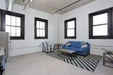 This single-floor residence showcases a compelling blend of industrial heritage and contemporary design. The living area is defined by painted white brick walls and black-framed windows that fill the space with natural light while offering open sky views. Polished concrete flooring runs throughout, reinforcing the unit's urban aesthetic.

The kitchen is well-appointed with white shaker-style cabinetry, granite countertops, and a full suite of stainless steel appliances, including a refrigerator, electric range, over-the-range microwave, and dishwasher. A stainless steel sink with a modern faucet completes the functional workspace, and an in-unit washer and dryer are also present.

The bedrooms feature neutral tones with soft carpeting underfoot. One bedroom benefits from exposed brick detailing and a large window, while the other offers a quieter, more streamlined feel with gray walls and clean finishes.

Two bathrooms serve the unit. One features tile flooring, a white vanity, and a walk-in shower, while the second includes a soaking tub, tiled floors, a white vanity with storage, and a black-framed window that brings in natural light. The overall ambiance is modern and industrial, with a cohesive palette of neutrals throughout.