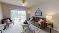 This single-floor residence offers a thoughtfully designed layout that balances comfort and functionality throughout its key living spaces. The living room serves as the heart of the home, featuring plush wall-to-wall carpeting, a ceiling fan, and large sliding glass doors fitted with vertical blinds that open to an outdoor patio, flooding the room with natural light and offering pleasant outdoor views. The adjacent dining area is an inviting space anchored by an elegant chandelier and neutral-toned walls, providing an ideal setting for meals and gatherings. The galley-style kitchen is well-equipped with warm oak cabinetry, granite-look countertops, a double sink, and white appliances including a range and dishwasher, with durable tile flooring underfoot. The primary bedroom is generously sized, featuring soft carpeting, a walk-in closet, and a window dressed with teal curtains that let in natural light. A second bedroom offers carpeted flooring and ample closet space, providing flexibility for guests or a home office. The full bathroom includes a combined tub and shower, a vanity with granite-look countertops, oak cabinetry, and tile flooring. Throughout the residence, neutral wall tones and consistent finishes create a cohesive and welcoming ambiance.