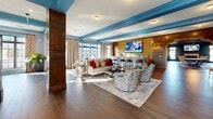 Located at 6899 Harlem Rd in Westerville, Ohio, this sophisticated two-story amenity facility makes a striking first impression with its grand lobby showcasing bold black-and-white marble checkerboard flooring, sky-blue wainscoting, and a sweeping staircase crowned by an ornate chandelier. A dramatic hand-painted accent wall adds artistic depth to the soaring entry. A reception desk with decorative fretwork paneling and floor-to-ceiling French doors connects to outdoor areas, flooding the space with natural light.

The main level houses a fully equipped fitness center and a state-of-the-art golf simulator room, complete with synthetic turf, a full-wall projection screen, and a comfortable lounge seating area. A dedicated private theater features tiered rows of plush navy velvet armchairs, coffered ceilings with rich wood tones highlighted in blue, crystal chandeliers, and curated wall art — creating an intimate, upscale cinematic experience.

The expansive upper floor, accessed by two staircases, offers rich dark hardwood flooring, blue-trimmed coffered ceilings, and abundant natural light through large steel-framed windows with exterior views. A sun-drenched lounge nook and a sophisticated conference room with a large boardroom table complete this level, making the space equally suited for relaxation and professional gatherings.