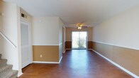Located at 6000 Mabeline Road in Hanahan, South Carolina, this two-story home offers a welcoming and functional layout designed for comfortable everyday living. The main living area immediately draws attention with its rich, dark hardwood-style flooring that runs throughout, creating a warm and cohesive aesthetic. A distinctive two-tone wall treatment — featuring a deeper tan lower half paired with a lighter cream upper half — adds a classic, structured character to the interior. A ceiling fan centered in the living room provides both practicality and a finishing touch to the space. Natural light flows generously into the room through a large sliding glass door, which also provides direct access to the outdoors, offering views of the surrounding greenery. The clean white trim and baseboards throughout complement the warm color palette, lending the space a tidy, well-maintained appearance. The two-floor layout provides ample room for living, with spaces distributed across both levels to accommodate a variety of needs. Overall, the home presents a bright, inviting atmosphere with durable finishes and thoughtful design details that make it a practical and comfortable residence in the Hanahan community.