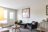 Located at 405 Sidney St in Quinte West, Ontario, this single-floor, two-bedroom, one-bathroom unit offers a well-organized layout that maximizes its compact footprint. The interior is finished with hardwood-style flooring throughout the main living areas, neutral grey-toned walls, and white trim, creating a clean and cohesive aesthetic.

The central hallway connects all rooms efficiently, with a dedicated closet providing additional storage. The living area benefits from natural light through windows that overlook greenery outside. The galley-style kitchen features white shaker cabinetry with brushed nickel hardware, marble-look countertops, a stainless steel refrigerator, and a coil-top range, all set atop light grey tile flooring — a practical and attractive space for everyday cooking.

The primary bedroom accommodates a full-sized bed comfortably and includes a built-in sliding door wardrobe with ample storage. A window allows natural light to fill the room. The second bedroom, also naturally lit with an outdoor window view, offers a cozy and functional space. The bathroom is finished in neutral grey tones and includes a full bathtub with a shower combination. Throughout, the unit maintains a bright, tidy, and functional character.