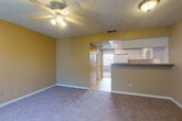 This single-floor unit features a straightforward, efficient layout connecting a carpeted living area, a kitchen, a bedroom, and a bathroom. The living room is finished with plush carpet, warm golden-yellow walls, and a textured ceiling. A ceiling fan with an integrated light fixture provides both ventilation and overhead lighting. An open passthrough connects the living room to the kitchen, creating a sense of openness between the two spaces.

The kitchen is well-equipped with white cabinetry offering ample storage, laminate countertops, and a full suite of white appliances including a refrigerator, electric range, dishwasher, and an overhead range hood. Light ceramic tile flooring runs throughout the kitchen and entry areas. A window above the sink area allows natural light to brighten the workspace.

The bedroom is generously sized, featuring the same warm-toned walls and soft carpet as the living area. A large window dressed with vertical blinds admits natural light and provides outdoor views. A closet with a paneled door offers convenient storage.

The bathroom includes a combined tub and shower unit, a vanity with storage, and light ceramic tile flooring, maintaining a clean, functional aesthetic consistent with the rest of the unit.