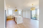 Located along S Federal Highway in Boynton Beach, FL, this thoughtfully designed two-bedroom, two-bathroom residence offers a refined contemporary aesthetic throughout. Light wood-look flooring flows across the open-concept main living area, anchored by a stunning kitchen featuring white cabinetry with brushed gold hardware, a marble-veined quartz island, stainless steel appliances, and a marble backsplash. Gold pendant lighting adds warmth and elegance to the space. Floor-to-ceiling sliding glass doors in the living area flood the interior with natural light and open to a curved balcony offering sweeping panoramic views of the Boynton Beach skyline and surrounding landscape. The hallway connects the living spaces to the private quarters via louvered closet doors, adding a classic architectural detail. The primary bedroom, a generously sized retreat, features plush carpeting and direct balcony access through full-height glass doors with expansive outdoor views. A walk-in closet with wire shelving provides ample storage. The primary bathroom is elegantly appointed with dual under-mount sinks set in quartz countertops, gold fixtures, white cabinetry, and a glass-enclosed walk-in shower. The second bedroom is carpeted and bright, accompanied by its own closet. Clean white walls and modern finishes throughout create a bright, cohesive ambiance.
