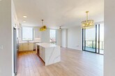 Located along S Federal Highway in Boynton Beach, FL, this thoughtfully designed two-bedroom, two-bathroom residence offers a refined contemporary aesthetic throughout. Light wood-look flooring flows across the open-concept main living area, anchored by a stunning kitchen featuring white cabinetry with brushed gold hardware, a marble-veined quartz island, stainless steel appliances, and a marble backsplash. Gold pendant lighting adds warmth and elegance to the space. Floor-to-ceiling sliding glass doors in the living area flood the interior with natural light and open to a curved balcony offering sweeping panoramic views of the Boynton Beach skyline and surrounding landscape. The hallway connects the living spaces to the private quarters via louvered closet doors, adding a classic architectural detail. The primary bedroom, a generously sized retreat, features plush carpeting and direct balcony access through full-height glass doors with expansive outdoor views. A walk-in closet with wire shelving provides ample storage. The primary bathroom is elegantly appointed with dual under-mount sinks set in quartz countertops, gold fixtures, white cabinetry, and a glass-enclosed walk-in shower. The second bedroom is carpeted and bright, accompanied by its own closet. Clean white walls and modern finishes throughout create a bright, cohesive ambiance.
