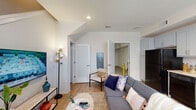 Located on Hillsborough Street in Raleigh, North Carolina, this three-story residence is thoughtfully designed across multiple levels connected by a staircase with clean white railings. The ground floor includes a private garage with a roll-up door and an on-site water heater, providing secure parking and functional utility space with a concrete floor.

The main living level features an open-concept layout where the living room and kitchen flow together seamlessly. The living area showcases light hardwood-style flooring, recessed lighting, and vaulted ceilings that lend a sense of openness. The kitchen is outfitted with gray shaker-style cabinetry, granite countertops, black appliances including a refrigerator, dishwasher, and range, and a window that brings in natural light. A built-in desk area adds a practical workspace within the kitchen.

The bedrooms are carpeted for comfort and feature vaulted or elevated ceilings with ceiling fans. At least one bedroom includes an en-suite bathroom, while additional bathrooms throughout the home are finished with gray vanities, granite countertops, hardwood-style flooring, and tub-shower combinations. The neutral white walls and consistent finishes across all floors give the space a cohesive, modern aesthetic.