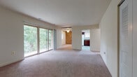 This single-floor residence offers a thoughtfully designed layout that balances open living spaces with comfortable private quarters. The expansive living area is finished with neutral wall-to-wall carpeting and features large sliding glass doors that open to a private balcony overlooking a tree-lined backdrop, filling the space with abundant natural light. An adjacent dining area adds character with exposed ceiling beams, a ceiling fan, and a striking brick accent wall that provides a warm, classic contrast to the otherwise light and airy interior.

The kitchen is efficiently laid out and separated from the living area by a peninsula counter with a dark granite-style surface. Rich dark wood cabinetry pairs with white appliances, including a refrigerator, range, and dishwasher, while tile flooring and a skylight-style overhead fixture keep the space bright and practical.

The bedrooms are generously sized, each carpeted and featuring natural light through well-placed windows. The primary bedroom includes an expansive set of double bi-fold closet doors offering ample storage, while a secondary bedroom also benefits from a large closet. The bathroom is clean and functional, finished with white tile flooring, a full soaking tub with shower, and a dark wood vanity consistent with the home's design palette.