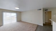 This single-floor residential unit offers a well-organized layout with a clear separation between living, sleeping, and functional spaces. The living room is a comfortable, open area finished with plush wall-to-wall carpeting and neutral beige walls that create a calm, welcoming atmosphere. A sliding glass door with vertical blinds fills the space with natural light while providing direct access to an outdoor patio area. The room transitions seamlessly into the entryway, where durable wood-look flooring begins and a pass-through counter connects to the kitchen.

The galley-style kitchen is efficiently designed with rich dark espresso cabinetry lining both walls, granite-look countertops, a double stainless steel sink, and white appliances including a range, dishwasher, and refrigerator. A pendant light adds a finishing touch to the adjacent dining area.

The unit includes two bedrooms, each carpeted and finished with neutral tones. Both rooms feature ceiling fans with light fixtures, and one bedroom benefits from a window that invites natural light and outdoor views.

The bathroom is clean and functional, featuring a full tub-shower combination with built-in shelving, a granite-top vanity with dark wood cabinetry, and wood-look tile flooring. Central HVAC vents are present throughout, ensuring year-round climate comfort.