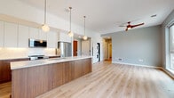 Located at 2416 Scranton Rd in Cleveland's vibrant Ohio City neighborhood, this modern single-floor residence offers a thoughtfully designed open-concept layout finished with contemporary details throughout. Light hardwood flooring flows seamlessly across the living and sleeping areas, lending a warm, cohesive feel to the entire space.

The kitchen serves as the centerpiece of the main living area, anchored by a substantial island with rich walnut-toned cabinetry and a crisp white quartz countertop. Upper cabinetry is finished in white with a marble-look tile backsplash, complemented by stainless steel appliances including a full-size refrigerator, built-in microwave, and range. A trio of globe pendant lights suspended on brass fixtures adds a stylish, modern touch.

The open living area benefits from large windows that invite ample natural light and offer views of the surrounding neighborhood. A ceiling fan with a sleek wood finish provides both form and function. The bedrooms continue the same light flooring and cool-toned gray walls, each equipped with ceiling fans and generously sized windows framing neighborhood views.

The bathroom features floor-to-ceiling marble-look tile surrounding a soaking tub and shower combination, with neutral floor tile and clean chrome fixtures. An in-unit stacked washer and dryer adds everyday convenience, rounding out this well-appointed modern residence.