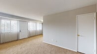 Located at 11431 Lockwood Dr in Silver Spring, MD, this single-floor residence offers a practical and well-organized layout designed for comfortable everyday living. The spacious living area is carpeted in warm beige tones and filled with natural light through large floor-to-ceiling vertical blinds that frame a full-length exterior door, creating an open and airy atmosphere. The neutral gray walls throughout provide a clean, versatile backdrop adaptable to a variety of interior styles. The kitchen features warm honey-toned wood cabinetry, light countertops, a stainless steel sink, and a full-size refrigerator, all set on hardwood-style flooring that adds a touch of contrast to the otherwise neutral palette. The bedrooms are generously sized, each finished with soft carpeting and windows fitted with blinds that allow for natural light and privacy. Multiple doorways and closet spaces within the bedroom areas contribute to the unit's functional design. The bathroom is finished with white tile surrounding a full tub-shower combination, maintaining a clean and straightforward aesthetic. Overall, this single-level residence presents a bright, move-in ready space with consistent finishes and a well-proportioned floor plan suited for a range of occupants.
