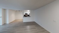 This single-floor residence offers a thoughtfully designed layout that balances functionality with a clean, contemporary aesthetic. The open-concept living area is spacious and filled with natural light, courtesy of large windows dressed with vertical blinds. Light-toned laminate wood flooring flows consistently throughout the unit, lending a cohesive and modern feel to every room.

The galley-style kitchen is efficiently organized with crisp white cabinetry, dark countertops, and a full suite of stainless steel appliances, including a gas range, microwave, refrigerator, and a stainless steel sink. A pass-through peninsula connects the kitchen to the living area, creating an open and accessible layout ideal for everyday use.

The bedroom is a well-proportioned, quiet space featuring a wide window with vertical blinds that diffuse natural light softly throughout the room. A mirrored sliding closet door adds depth and reflects light, enhancing the sense of space.

The bathroom is neatly appointed with a white vanity, dark countertop, integrated sink, large mirror, and chrome hardware including a grab bar, combining practicality with clean design. Textured ceilings are found throughout the unit, and track lighting in the living area provides versatile illumination. Overall, the space presents a bright, neutral palette ideal for comfortable everyday living.
