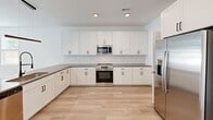 Located at 2165 Casablanca Way in Knoxville, Tennessee, this two-story home offers four bedrooms and four bathrooms across two well-proportioned floors of nearly equal size. The main level features an open-concept kitchen and living room with light wood-tone flooring, white cabinetry, stainless steel appliances including a side-by-side refrigerator, and recessed lighting. A dedicated pantry provides additional storage, while sliding glass doors lead to a patio with a black metal railing and outdoor views. A hallway with a barn-style sliding door connects the main living areas seamlessly. The attached garage includes an automatic opener and houses the electrical panel. Upstairs, four spacious bedrooms feature the same warm wood flooring and ceiling fans with light fixtures. The generously sized primary bedroom includes a walk-in closet outfitted with wire shelving. Three additional closets offer ample storage throughout. The four bathrooms are finished with white subway tile surrounds, black hardware accents, and wood-look flooring, maintaining a clean, cohesive aesthetic. Hallways on both levels are bright and well-connected. The exterior showcases a modern board-and-batten facade, complementing the home's crisp, contemporary interior design.