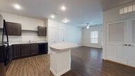 Located at 1530 Marbach Oaks in San Antonio, Texas, Unit 4304 is a single-floor residence featuring a cohesive, modern design throughout. Rich, dark hardwood-style flooring runs consistently across the living spaces, creating a warm and grounded aesthetic complemented by crisp white walls and clean baseboards.

The open-concept living area is generously proportioned, benefiting from natural light streaming through horizontal-blind-covered windows and a glass door that leads to an exterior exit. Ceiling fans are present in the main living spaces, providing both functionality and a finishing touch to each room.

The kitchen is well-appointed with dark espresso-toned cabinetry, light granite-style countertops, a full suite of black appliances including a refrigerator, range, microwave, and dishwasher, and a tiled backsplash. A central kitchen island with a matching countertop provides additional workspace and casual dining potential. A distinctive built-in arched nook with a desk surface offers a dedicated workspace area just off the kitchen.

The bedroom is spacious and bright, featuring the same hardwood-style flooring and a ceiling fan, with direct access to a private bathroom. The bathroom includes a soaking tub with white tile surround, a vanity with granite-style countertops, and dark cabinetry consistent with the kitchen's design language. Additional storage is accessible via a louvered-door closet near the workspace nook.