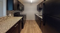 This single-floor residence offers a thoughtfully designed layout that balances comfort and functionality. The entryway greets visitors with wood-look plank flooring and a coat closet, opening seamlessly into the main living area. The living and dining spaces flow naturally together, with soft carpet underfoot, a ceiling fan, and access to natural light through a large window with vertical blinds.

The galley-style kitchen is a standout feature, lined on both sides with rich, dark espresso cabinetry accented by brushed chrome hardware and a decorative tile backsplash. Granite-style countertops provide ample workspace, and the kitchen is equipped with black appliances including a range, microwave, refrigerator, and a sink with a modern faucet. Wood-look flooring continues throughout this space, adding warmth and cohesion.

The two bedrooms are generously sized, each featuring plush wall-to-wall carpet, neutral warm-toned walls, sliding double-door closets, and windows that invite natural light. The textured ceilings add a classic touch throughout the home.

Both bathrooms are clean and functional, featuring wood-look tile flooring, dark vanity cabinetry with granite-style countertops, and a tub-shower combination with white subway-style tile surround. The overall ambiance is neutral, bright, and move-in ready.