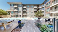Located at 12639 Coit Rd in Dallas, TX, this contemporary multi-story residential community showcases a striking blend of stucco and brick exterior facades with clean, modern lines. The complex is designed around a central courtyard that serves as the focal point of outdoor living, featuring a generously sized resort-style swimming pool with crystal-clear turquoise water, complemented by a separate spa or wading pool nearby. Rows of sleek lounge chairs line the pool deck, providing ample space for relaxation under the Texas sun. A thoughtfully landscaped walkway leads through the courtyard, accented by decorative planters, native grasses, river rock, and mature trees that add shade and natural beauty to the setting. Outdoor dining areas with tables and chairs are integrated throughout the courtyard, creating inviting spaces for social gatherings. Each floor of the surrounding building features private balconies, offering residents elevated views of the vibrant courtyard below. Large windows throughout the facade allow for abundant natural light within individual units. The overall ambiance is that of a well-appointed, amenity-rich community that balances modern design with comfortable, resort-inspired outdoor living in the heart of North Dallas.