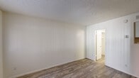Located at 1150 West University Drive in Tempe, Arizona, this compact single-floor unit offers an efficient and straightforward layout designed for practical living. The space consists of a living area, a kitchenette, and a full bathroom, all finished with consistent wood-look plank flooring that runs throughout, lending a cohesive and easy-to-maintain aesthetic.

The living area features crisp white walls with subtle vertical paneling detail on one side, a textured popcorn ceiling, and a window that allows natural light to filter in, brightening the otherwise neutral interior. The entry door is positioned adjacent to the window, creating a simple and functional entryway directly into the main living space.

The kitchenette area, visible in the dollhouse view, includes a sink and cabinetry, providing basic cooking and prep functionality within a compact footprint.

The bathroom is well-appointed for its size, featuring wood-look flooring that matches the rest of the unit, a toilet, a vanity with a countertop sink, a medicine cabinet with mirror, and a walk-in shower enclosed by a sliding glass door. A flush-mounted ceiling light provides adequate illumination throughout.

Overall, the unit presents a clean, no-frills environment suited for single occupancy, conveniently situated near Arizona State University in central Tempe.