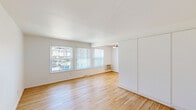 This single-floor, 2-bedroom, 1-bathroom unit offers a well-organized and efficient layout. Warm hardwood floors run throughout the space, creating a cohesive feel from room to room. The living area is bright and open, featuring multiple windows dressed with vertical blinds that allow generous natural light to filter in, along with a ceiling fan and a wall-mounted AC unit for year-round comfort. A large built-in storage unit along one wall adds practical functionality. The entry area provides a clean transition into the main living space, anchored by a classic wood-tone front door. Both bedrooms are comfortably sized with hardwood floors and windows that bring in natural light; the primary bedroom includes a built-in closet with dual hanging rods and shelving. The kitchen is equipped with white cabinetry, a gas range, refrigerator, and a double sink with ample counter space — offering everything needed for everyday cooking. The bathroom is a standout feature, showcasing retro mint-green wall tiles with contrasting navy border tiles, a full bathtub with shower, and a window for natural ventilation. A connecting hallway ties all rooms together, completing this practical and charming layout.