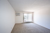 This single-floor residential unit offers a well-organized layout with distinct living, sleeping, and cooking areas. The living room is generously sized, finished with wall-to-wall carpet, a textured ceiling, and a large sliding glass door fitted with vertical blinds that floods the space with natural light and provides outdoor access. Adjacent to the living area, the galley-style kitchen is efficiently designed with warm oak cabinetry lining both walls, light-toned countertops, a double sink, tile flooring, and white appliances including a range and refrigerator. The bedrooms are carpeted and bright, each featuring ceiling fans with integrated lighting, windows with horizontal blinds that bring in natural views of surrounding greenery, and baseboard heating. One bedroom includes a built-in closet with sliding wood-panel doors and direct access to an adjoining room or bathroom. Throughout the unit, consistent warm wood trim accents the windows, doors, and baseboards, contributing to a cohesive and understated interior aesthetic. The textured ceilings are a recurring architectural detail across the living and sleeping spaces. Overall, the unit presents a functional and comfortable floor plan suited for everyday residential living.