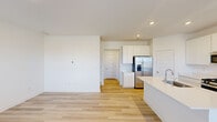 This clean, contemporary two-story home is designed with a bright, open layout and a neutral color palette throughout. The main living area flows seamlessly into a well-appointed kitchen, which serves as the heart of the home. The kitchen features a large center island with an integrated sink, crisp white shaker cabinetry extending to the ceiling, and a full suite of stainless steel appliances including a gas range, built-in microwave, and a French door refrigerator with an in-door ice and water dispenser. Light-toned hardwood flooring runs throughout the main level, enhancing the airy, open feel of the space. Recessed lighting provides consistent, modern illumination throughout the kitchen and living areas. The upper level hosts multiple bedrooms, each finished with plush neutral carpet and windows fitted with blinds that allow for natural light while maintaining privacy. The bathroom is outfitted with a full-size soaking tub and shower combination with chrome fixtures and tile flooring. Additional rooms on the second floor offer versatile space with hardwood flooring and windows overlooking the surrounding neighborhood. The overall design of this home emphasizes a clean, move-in-ready aesthetic with thoughtful finishes throughout both levels.