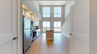 This contemporary two-story residence makes an immediate impression with its dramatic double-height ceilings in the main living area, where floor-to-ceiling windows flood the space with natural light and frame sweeping city views. The open-concept layout connects the living area seamlessly to a well-appointed kitchen featuring crisp white shaker cabinetry, granite countertops, a central island, and a full suite of stainless steel appliances including a refrigerator, electric range, over-the-range microwave, and dishwasher. Light wood-tone flooring runs throughout the main level, enhancing the bright and airy atmosphere. A staircase leads to the upper level, where carpeted bedrooms provide a comfortable retreat. The primary bedroom includes direct access to a private en-suite bathroom equipped with a glass-enclosed walk-in shower and a granite-topped vanity. A secondary bathroom on the lower level offers a full soaking tub with a white subway tile surround and a matching granite vanity. An additional carpeted room on the upper level opens directly to a private outdoor area, adding versatile indoor-outdoor living to this well-designed, light-filled space.