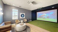 Located in Summerfield, FL, this dedicated indoor sports simulator room offers a compelling blend of high-tech recreation and comfortable lounge space within a compact, efficiently designed footprint. The room is divided into two functional zones: an active playing area and a relaxed seating lounge.

The simulator zone features a lush artificial turf surface, dark acoustic wall panels, and a ceiling-mounted black tile enclosure that creates an immersive playing environment. A large, high-definition projection screen dominates the far wall, powered by a ceiling-mounted projector, and supports a variety of sports simulations including golf and soccer. Wall-mounted shelving displays an assortment of sport balls, and a control station with a monitor allows users to easily navigate the simulator's interface.

The lounge area transitions seamlessly from the simulator zone via light hardwood-style flooring. Two streamlined upholstered sofas and a pair of patterned accent chairs are arranged around a round concrete-style ottoman atop a textured area rug. A framed circular artwork adds a decorative focal point to the grey-toned walls, while a window provides natural light. Posted simulator rules and a wall-mounted TV complete the space, making it both functional and inviting for players and spectators alike.