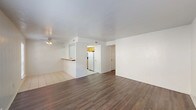 This single-story space is thoughtfully laid out, offering a functional and comfortable living environment across several well-defined areas. The open living area immediately draws attention with its rich, dark hardwood-style flooring and textured ceiling, providing a clean, neutral backdrop. Large windows along the front of the living space allow generous natural light to fill the room, with views of surrounding greenery. A ceiling fan with integrated lighting serves both the living and dining areas efficiently.

The kitchen is positioned adjacent to the living space and is accessible via a half-wall breakfast bar. It features warm oak cabinetry, granite-style tile countertops, a white electric coil range with an overhead ventilation hood, and a white refrigerator. Light tile flooring carries through this area seamlessly.

The bedrooms are carpeted in a neutral tan tone and each include ceiling fan light fixtures. One bedroom features a wide window with blinds, while another includes closet access and a door leading to additional hallway space.

Two bathrooms serve the unit, each equipped with oak vanity cabinetry, white countertops with integrated sinks, large mirrors, and light tile flooring. The layout ensures practical access between the bedrooms and bathrooms, contributing to a well-organized overall flow throughout the space.