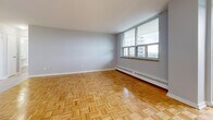 Located at 1001 Main St W in Hamilton, Ontario, this one-bedroom, one-bathroom unit offers a well-organized layout across a single floor. The open-concept living and dining area is immediately inviting, featuring warm parquet wood flooring in a classic herringbone pattern that runs throughout the main living spaces. Large windows flood the area with natural light and frame views of the Hamilton cityscape and surrounding greenery, creating a bright and airy atmosphere. Baseboard heating runs along the exterior walls beneath the windows, ensuring year-round comfort.

The kitchen is efficiently designed with white cabinetry extending to the ceiling for ample storage, granite-style countertops, a stainless steel sink, and a white range. Light-toned tile flooring distinguishes the kitchen from the living area. The entrance provides a practical transition into the unit with access to both the main living space and adjacent rooms.

The bedroom is a well-proportioned retreat, continuing the parquet flooring, with a large window offering city views and a built-in double closet for generous storage. The bathroom is clean and straightforward, featuring a full-sized soaker tub with white tile surround. Overall, the unit presents a functional and comfortable living space in a convenient Hamilton location.