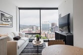 This thoughtfully designed one-bedroom, one-bathroom unit in the heart of Boise, ID offers a bright and modern living experience with a clean, contemporary aesthetic throughout. The open-concept layout seamlessly connects the kitchen, dining, and living areas, maximizing the efficient use of space. The kitchen is outfitted with stainless steel appliances, including a gas range, dishwasher, and French door refrigerator, complemented by light wood cabinetry extending to the ceiling and a white tile backsplash. Light hardwood flooring runs throughout the main living area, enhancing the airy atmosphere. The living room is anchored by dramatic floor-to-ceiling windows that frame sweeping views of the Boise skyline and surrounding foothills, flooding the space with natural light. The bedroom offers a serene retreat with a generous closet featuring built-in shelving and its own large window overlooking the cityscape. The bathroom includes a combined tub and shower with tile surround, a single vanity with wood cabinetry, and a backlit mirror. An entry hallway with additional storage completes this well-appointed urban unit, ideal for those seeking modern comfort in a prime downtown Boise location.