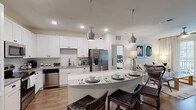 This thoughtfully designed single-floor residence offers a seamless blend of modern finishes and functional living spaces. The kitchen serves as the heart of the home, showcasing crisp white shaker cabinetry, granite countertops, a classic subway tile backsplash, and a full suite of stainless steel appliances including a French door refrigerator, electric range with over-the-range microwave, and dishwasher. A curved kitchen island with pendant lighting provides additional seating and prep space, flowing naturally into the main living area.

The multiple bedrooms are bright and comfortable, each featuring plush carpeting, ceiling fans, and generously sized windows that invite abundant natural light and views of lush outdoor greenery. The rooms offer ample space for full bedroom furniture arrangements.

The bathrooms are finished to a high standard, featuring white cabinetry, granite countertops, and undermount sinks. The primary bathroom includes a dual-sink vanity with a large framed mirror, while a secondary bathroom features a combined tub and shower with subway tile surround and direct access to a walk-in closet with built-in shelving. Wood-look flooring runs throughout the main living areas, adding warmth and cohesion to the overall aesthetic.