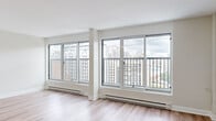 Located at 3474 Rue Hutchison in Montreal's vibrant Mile End neighbourhood, this well-appointed unit offers a bright and modern living environment across a single floor. The layout is defined by an abundance of natural light, courtesy of large floor-to-ceiling windows that frame impressive panoramic views of the Montreal skyline and Mont Royal beyond.

Light wood flooring runs throughout the main living areas, lending warmth and continuity to the open-concept spaces. The spacious living and dining areas are particularly striking, with banks of wide windows fitted with Juliet-style balcony railings that draw the eye outward to the cityscape. Baseboard heating runs along the window walls, ensuring year-round comfort.

The kitchen is compact yet functional, featuring a two-tone cabinetry design with white upper cabinets and dark wood lower cabinets, stainless steel appliances including a refrigerator and electric range, a tile backsplash, and ample overhead storage. The bedroom benefits from its own generous window with the same sweeping city views, maintaining the airy feel found throughout the unit. A clean, minimalist bathroom completes the space, outfitted with a dark wood vanity, integrated sink, tile flooring, and a walk-in shower. The overall aesthetic is fresh, neutral, and move-in ready.