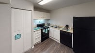 This single-story unit offers a practical and cohesive layout spread across several well-defined living areas. Dark hardwood-style flooring runs consistently throughout the space, providing a warm, grounding contrast to the neutral gray walls and white trim found in every room. Textured ceilings are present throughout, adding a classic architectural detail.

The kitchen is efficiently arranged in an L-shaped configuration, featuring white cabinetry that extends to the ceiling for ample storage, light-toned countertops, and a full suite of black appliances including an electric range, dishwasher, and refrigerator. A built-in sink with a window-adjacent position and a louvered bi-fold closet door add to the kitchen's functionality.

The living area is generously sized and receives natural light through a large sliding glass door fitted with vertical blinds, offering outdoor access. Additional rooms, likely serving as bedrooms, are well-proportioned with neutral walls and windows that bring in natural light. One room features a louvered bi-fold closet. The overall ambiance of the unit is clean, understated, and move-in ready, with a consistent design language tying each space together.