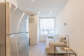 Located at 695 Niagara St in Welland, Ontario, this thoughtfully designed single-floor unit makes efficient use of its compact footprint across three well-defined areas. The open-concept kitchen and living space anchors the layout, showcasing crisp white cabinetry with brushed nickel hardware, light quartz countertops, and a full suite of stainless steel appliances including a refrigerator, electric range, over-the-range microwave, and dishwasher. A double stainless steel sink adds practicality, while recessed lighting illuminates the space from above. Light-toned luxury vinyl plank flooring runs continuously throughout, lending warmth and visual continuity. A compact dining nook with a bistro-style table sits adjacent to the kitchen, and the living area at the far end benefits from a large window fitted with a roller blind, drawing in natural light. The bedroom is a calm, minimalist retreat with neutral white walls, recessed lighting, a window with outdoor views, and a double closet with paneled doors. The bathroom is finished in all-white with a full soaker tub and shower combo, built-in shelving, and clean chrome fixtures. The overall aesthetic is modern and understated, offering a functional, move-in-ready living space.