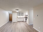 This well-appointed 2-bedroom, 1-bathroom residence in Sioux Falls, South Dakota offers a comfortable and functional single-floor layout. The spacious living room is a standout feature, showcasing durable wood-style plank flooring, a wall-mounted air conditioning unit, baseboard heating, and a sliding glass door that opens to a private balcony overlooking mature trees—filling the space with natural light and greenery.

The galley-style kitchen is efficiently designed with white shaker cabinetry, granite-style countertops, stainless steel appliances including a refrigerator, microwave, and electric range, and a deep sink. An adjacent dining or flex area features additional white cabinetry with glass-front upper cabinets and under-cabinet lighting, providing generous storage and display space.

Both bedrooms are carpeted for comfort and include windows with outdoor views, baseboard heating, and ample closet space with sliding panel doors. The primary bedroom also features a ceiling fan. The full bathroom is clean and functional, offering a white vanity with storage, a tub/shower combination, and wood-style flooring that ties the space together cohesively.

Neutral warm tones and textured ceilings are consistent throughout, creating a bright and inviting atmosphere suited for comfortable everyday living.
