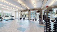 Located at 1231 Arya Way in Ocoee, Florida, this single-floor fitness center is a well-appointed, modern facility designed to inspire and accommodate a wide range of workout routines. The space is defined by its bright, open layout and an abundance of natural light streaming in through large windows and floor-to-ceiling glass garage doors that open directly to an outdoor courtyard, creating a seamless indoor-outdoor connection and views of the surrounding community.

The flooring throughout features a stylish combination of light wood-tone and blue tile accents, adding a dynamic visual element to the space. Overhead, industrial-style fluorescent lighting provides consistent illumination across the entire facility.

A striking, large-scale branded mural anchors one wall, rendered in deep blues and teals with motivational phrases — "work hard, make it happen" and "challenge yourself everyday" — serving as a bold focal point that energizes the environment.

Equipment is thoughtfully distributed across the space and includes treadmills, stationary and air-assault bikes, elliptical machines, rowing machines, free weights and a dumbbell rack, medicine balls, stability balls, a functional training rig with TRX suspension systems, and additional strength accessories. The open floor plan allows ample room for stretching and functional movement, making this a comprehensive, inviting fitness destination.