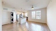 This single-floor unit in Jacksonville, Florida offers a thoughtfully arranged open-concept layout that maximizes its compact footprint. Light wood-look flooring runs continuously throughout the space, creating visual cohesion and a warm, clean aesthetic.

The combined kitchen and living area forms the heart of the unit. The kitchen is well-appointed with white shaker-style cabinetry, granite countertops, a white subway tile backsplash, and a full suite of stainless steel appliances including a refrigerator, range, microwave, and dishwasher. A central island with a granite top and pendant lighting overhead serves as both a prep surface and a casual dining spot. The living area benefits from two large windows that admit generous natural light and provide views of the surrounding neighborhood. A ceiling fan is centrally positioned, enhancing airflow and comfort.

The bathroom features a wide vanity with granite countertops, a undermount sink, and ample cabinet and drawer storage, complemented by a tiled shower and wood-look flooring. A dedicated closet provides practical storage. A stacked washer and dryer unit is also included within the space, adding everyday convenience to this efficiently designed unit.