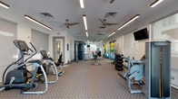 Located at 3281 Tutt Blvd in Colorado Springs, CO, this single-floor fitness center offers a comprehensive workout environment designed to accommodate a wide range of exercise needs. The space is thoughtfully laid out, with distinct zones dedicated to cardio, strength training, and functional fitness. Flooring throughout consists of durable patterned carpet, providing a comfortable surface across the entire facility.

The cardio section features Matrix-brand treadmills and elliptical trainers positioned near large windows fitted with roll-down shades, allowing natural light to filter in while maintaining privacy. Multiple wall-mounted flat-screen televisions are strategically placed throughout the room, ensuring visibility from various workout stations.

The strength training area includes a multi-station cable machine, a vertical knee raise tower, and a selection of selectorized weight machines. A well-organized free weight rack holds a full range of dumbbells, while an adjacent functional training corner stores stability balls in multiple sizes, resistance bands, foam rollers, and additional accessories on dedicated racks.

A floor-to-ceiling mirror along one wall visually expands the space and supports form-checking during workouts. Multiple ceiling fans and recessed linear lighting maintain a comfortable, well-lit atmosphere throughout. Exit doors on the far wall provide access to an exterior area, completing this practical and modern fitness facility.