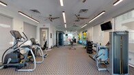 Located at 3281 Tutt Blvd in Colorado Springs, CO, this single-floor fitness center offers a comprehensive workout environment designed to accommodate a wide range of exercise needs. The space is thoughtfully laid out, with distinct zones dedicated to cardio, strength training, and functional fitness. Flooring throughout consists of durable patterned carpet, providing a comfortable surface across the entire facility.

The cardio section features Matrix-brand treadmills and elliptical trainers positioned near large windows fitted with roll-down shades, allowing natural light to filter in while maintaining privacy. Multiple wall-mounted flat-screen televisions are strategically placed throughout the room, ensuring visibility from various workout stations.

The strength training area includes a multi-station cable machine, a vertical knee raise tower, and a selection of selectorized weight machines. A well-organized free weight rack holds a full range of dumbbells, while an adjacent functional training corner stores stability balls in multiple sizes, resistance bands, foam rollers, and additional accessories on dedicated racks.

A floor-to-ceiling mirror along one wall visually expands the space and supports form-checking during workouts. Multiple ceiling fans and recessed linear lighting maintain a comfortable, well-lit atmosphere throughout. Exit doors on the far wall provide access to an exterior area, completing this practical and modern fitness facility.