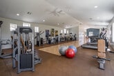 Located at 1466 Seminole Circle in Upland, California, this single-story fitness center offers a spacious and well-organized workout environment designed to accommodate a full range of exercise needs. The facility is defined by its elongated layout, which creates an open, unobstructed feel throughout the main workout area.

The flooring transitions between polished hardwood in the central open zone and durable rubber tile in the equipment areas, providing both aesthetic appeal and functional safety. Vaulted ceilings with a bold teal accent wall at the far end add architectural character, while ceiling fans and recessed lighting ensure a comfortable and well-lit environment. Large windows along the perimeter allow natural light to filter in and offer views of the surrounding greenery.

The cardio section features treadmills, ellipticals, stationary bikes, and stair climbers, while the strength training area is equipped with multiple cable machines, weight benches, and resistance equipment. Full-length mirrors at the rear wall enhance the sense of depth and aid in form monitoring.

A separate lounge area near the entrance includes seating with stylized industrial-frame chairs, framed artwork, and access to restrooms with mosaic tile accents and dual water fountains, rounding out the facility's functional amenities.