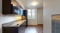 Located at 3635 Phinney Ave N in Seattle's vibrant Phinney Ridge neighborhood, Unit 13 is a thoughtfully designed single-floor unit that blends contemporary style with functional efficiency. The unit features warm wood-tone flooring throughout, creating a cohesive and inviting aesthetic across all areas.

The kitchen is a standout feature, outfitted with dark espresso cabinetry, a sleek countertop with an undermount sink, a built-in microwave, a full-size refrigerator, and a smooth cooktop surface. Upper and lower cabinetry provide ample storage, while a window above the counter allows natural light to fill the space and offers a view of the surrounding greenery.

The living and entry area is clean and minimal, featuring wall-mounted shelving brackets and a modern steel entry door. A recessed mailbox panel is integrated into the wall, adding a practical touch to the entryway.

The bathroom is efficiently designed with wood-tone flooring, a dark vanity cabinet with a white basin sink, a mirrored medicine cabinet, a toilet, and a bathtub with a shower — all presented in a clean, contemporary finish.

The bedroom is a bright, open room with neutral walls, wood flooring, and a standard door, offering a versatile and flexible space. Large windows throughout the unit ensure consistent natural light and a connection to the lush Seattle surroundings.