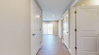 This single-floor unit is thoughtfully designed with a cohesive aesthetic carried throughout every room. Light wood-style luxury vinyl flooring runs continuously across the space, complemented by neutral greige wall tones and crisp white trim, creating a clean and contemporary feel.

The kitchen is a standout feature, outfitted with rich dark mahogany-style cabinetry, granite countertops, and a full suite of stainless steel appliances including a refrigerator with water dispenser, range, over-the-range microwave, and dishwasher. Recessed lighting illuminates the workspace effectively, and a window provides natural light.

The hallway connects multiple rooms and leads to a naturally lit living area at the far end, where vertical blinds cover a sliding or large window offering outdoor views. Panel-style white doors with brushed hardware are featured throughout, lending a polished look.

The bedrooms are generously sized with neutral walls and ample closet space, including a built-in shelving system visible in one bedroom. The bathroom features a granite-topped dark wood vanity, a tiled soaking tub and shower combination with large-format white tile, and wood-look flooring that continues the unit's consistent design language.