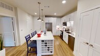 Located at 2240 SH 114 Frontage Rd in Trophy Club, Texas, this single-floor residence combines modern design with functional living spaces. The open-concept kitchen is a standout feature, showcasing crisp white shaker cabinetry, quartz countertops, and a full suite of stainless steel appliances including a French door refrigerator, electric range, microwave, and dishwasher. A decorative mosaic tile backsplash adds texture and visual interest, while warm wood-look flooring flows seamlessly throughout. A generously sized kitchen island with a built-in wine rack doubles as a dining area, illuminated by elegant pendant lighting overhead. The living area is bright and welcoming, with natural light streaming through large windows and access to an outdoor area. A ceiling fan and neutral tones create a comfortable, relaxed atmosphere. The bedroom is thoughtfully designed with a bold navy accent wall, large windows, a ceiling fan, and ample natural light, lending the room a calm and stylish character. The bathroom is finished with white cabinetry, quartz countertops, a large vanity mirror, and a tiled tub-shower combination, maintaining the clean, modern aesthetic found throughout the entire residence.
