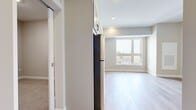 This thoughtfully designed one-bedroom, one-bathroom unit offers a clean, modern aesthetic throughout its efficiently organized single-floor layout. Light hardwood flooring flows through the main living and kitchen areas, complemented by neutral warm-gray walls that create a bright, welcoming ambiance.

The kitchen is a standout feature, equipped with a full suite of stainless steel appliances including a refrigerator, dishwasher, electric range, and over-the-range microwave. Gray shaker-style cabinetry with matte black hardware extends to the ceiling for ample storage, while light quartz countertops and a tile backsplash complete the contemporary look. A large window brings in generous natural light and outdoor views.

The living area continues the light hardwood flooring and receives additional natural light from a set of wide windows. The bedroom features plush carpeting, soft neutral tones, and a stylish frosted-glass sliding barn door that leads conveniently to the bathroom. The bathroom includes a full tub-shower combo, a wide vanity with white cabinetry and matte black fixtures, and a large mirror.

Additional highlights include a dedicated closet and an in-unit laundry area with a stacked GE washer and dryer, maximizing convenience within the compact footprint.
