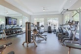 Located at 1800 Deerfield Pt in Milton, GA, this single-floor fitness center offers a spacious and thoughtfully designed workout environment. The facility is outfitted with a broad range of Matrix-brand equipment, including treadmills, ellipticals, cable machines, selectorized strength machines, and a full dumbbell rack, catering to a wide variety of fitness goals and training styles. Large, multi-pane windows line the walls, flooding the interior with natural light and providing pleasant views of the surrounding greenery — creating a bright and motivating atmosphere. Full-length mirrors are strategically placed throughout the space, enhancing the sense of openness while allowing users to monitor their form. The flooring consists of durable, cushioned rubber-composite material suited for high-traffic fitness use. A tray ceiling with recessed lighting and ceiling fans adds architectural detail and ensures the space remains well-lit and comfortable. The neutral, warm-toned walls and clean layout contribute to a professional yet welcoming ambiance. A transitional corridor connects the main workout floor to an adjacent area, suggesting additional amenity spaces nearby. Overall, this fitness center is designed to deliver a functional, well-appointed exercise experience in a comfortable and visually appealing setting.