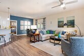 This thoughtfully designed 1-bedroom, 1-bathroom residence offers a comfortable and functional single-floor layout with warm wood-look flooring flowing throughout. The welcoming entrance leads into a spacious open-concept living and dining area, where neutral toned walls are accented by a bold teal feature wall that adds visual depth and character. The generously sized living room features a ceiling fan, ample natural light, and room for a full furniture arrangement. Adjacent to the living area, the dedicated dining space accommodates a full-sized dining table and opens to an outdoor area via glass doors, allowing for natural light and outdoor views. The peninsula-style kitchen offers warm wood cabinetry, stainless steel appliances, a countertop bar with seating, and track lighting overhead — ideal for both cooking and casual dining. The primary bedroom is a comfortable retreat with wood-look flooring and bright windows dressed with stylish curtains. The full bathroom is well-equipped with both a soaking tub and a separate glass-enclosed shower, finished with tile flooring and warm neutral tones. A dedicated laundry room houses a full-sized washer and dryer. A closet and entrance area complete this well-rounded, move-in-ready floor plan.