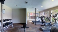 This single-floor fitness center is designed to provide a practical and comfortable exercise environment. The space is outfitted with multiple treadmills and a rowing machine, catering to a range of cardio-focused workout routines. Patterned carpet flooring in earthy tones covers the exercise area, adding a layer of warmth to the functional setting. Recessed lighting in the ceiling ensures consistent illumination throughout, complemented by generous natural light streaming in through large windows along the far wall. These windows offer views of an adjacent outdoor area, creating an open and airy atmosphere. The neutral-toned walls and clean layout contribute to an uncluttered, focused workout environment. A structural column positioned toward the center of the room subtly divides the space while maintaining an open feel. Ventilation is provided through ceiling-mounted HVAC vents, supporting a comfortable climate during exercise. Overall, the fitness center balances functionality with a welcoming ambiance, making it a well-suited facility for daily physical activity.